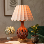 Decorative table lamp with a unique design on a wooden surface, surrounded by plants and a book.