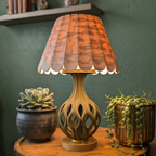 Decorative lamp with a wooden base and maroon lampshade on a wooden surface with two potted plants.