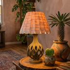 Decorative lamp with scalloped shade on a wooden table with plants in the background