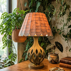 Decorative table lamp with a wooden base and pleated shade on a wooden surface with plants in the background.